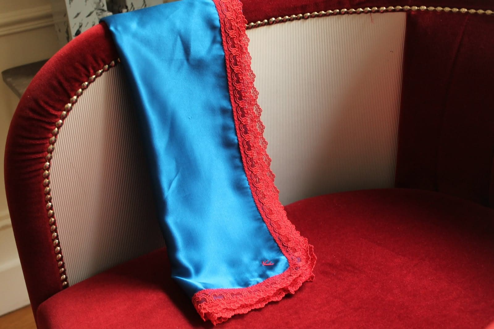 Foulard cobalt à dentelle rouge posé sur un fauteuil en velours rouge